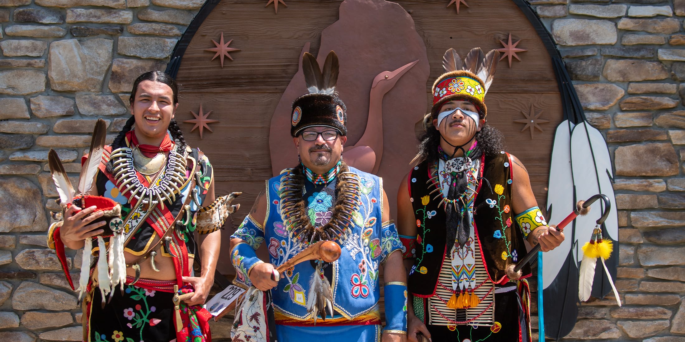 GLT-Inside-Hero24 A pow wow or celebration with 3 people dressed in regalia